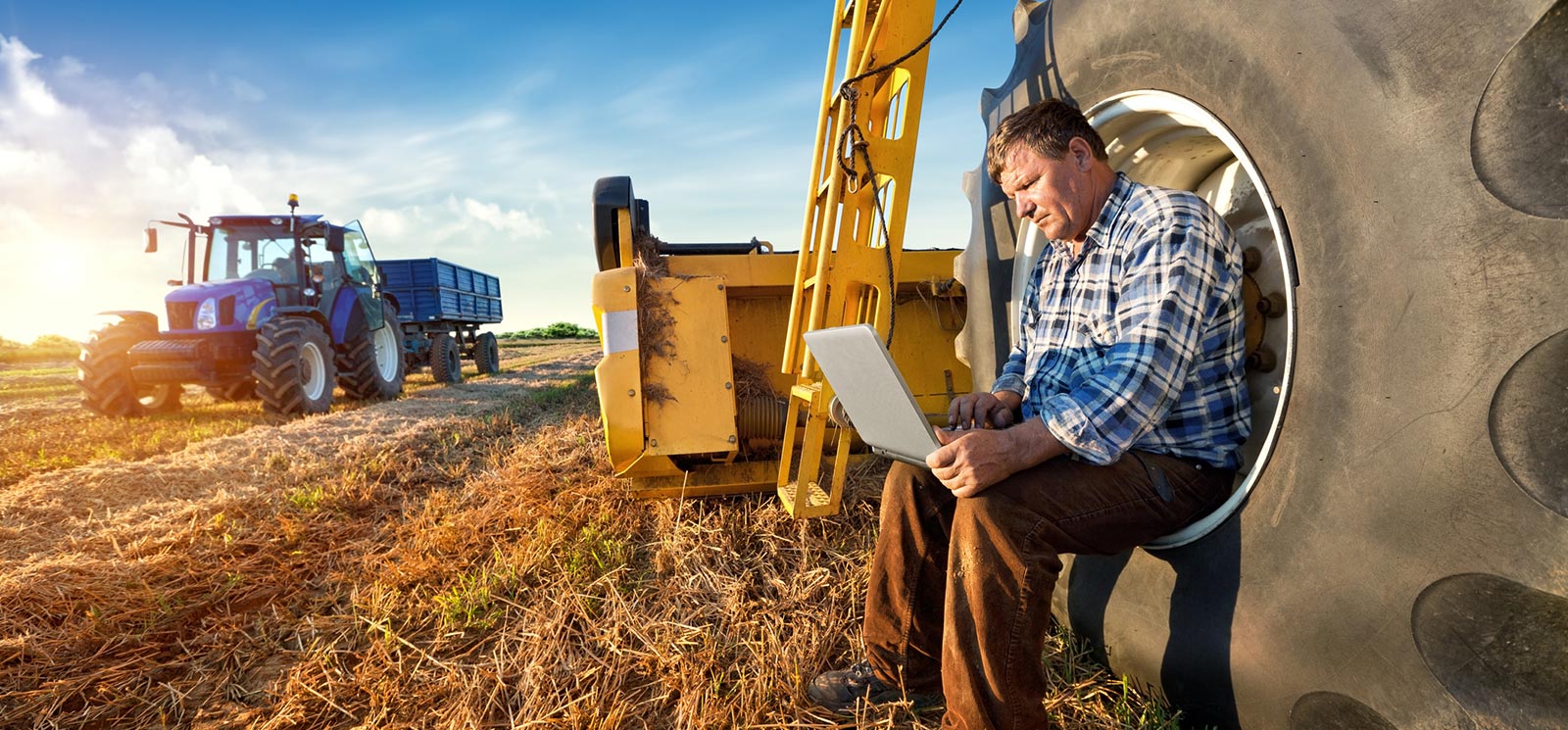 Farmer on a laptop computer with farming equipment
