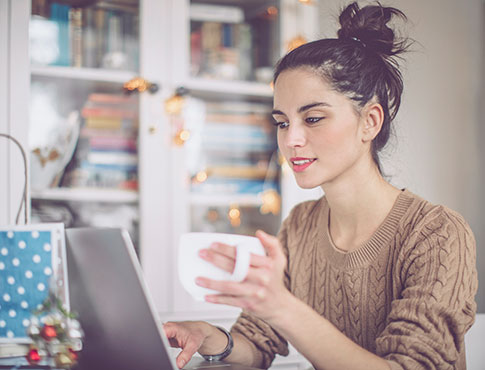 Lady drinking coffee while working on a laptop computer