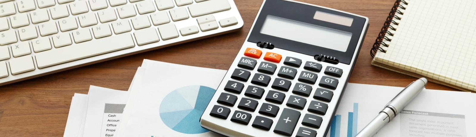 a calculator, writing pen, a keyboard and a note pad laying on a desk